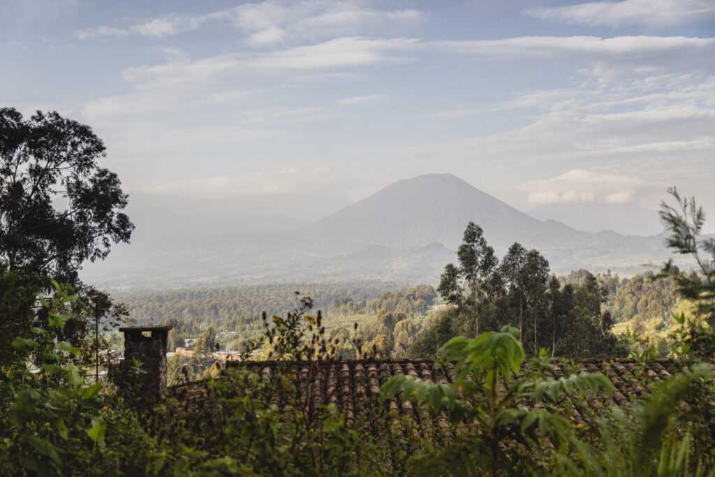 Volcano-shaped mountain rising over a valley, seen from a foreground of trees and a tiled roof.