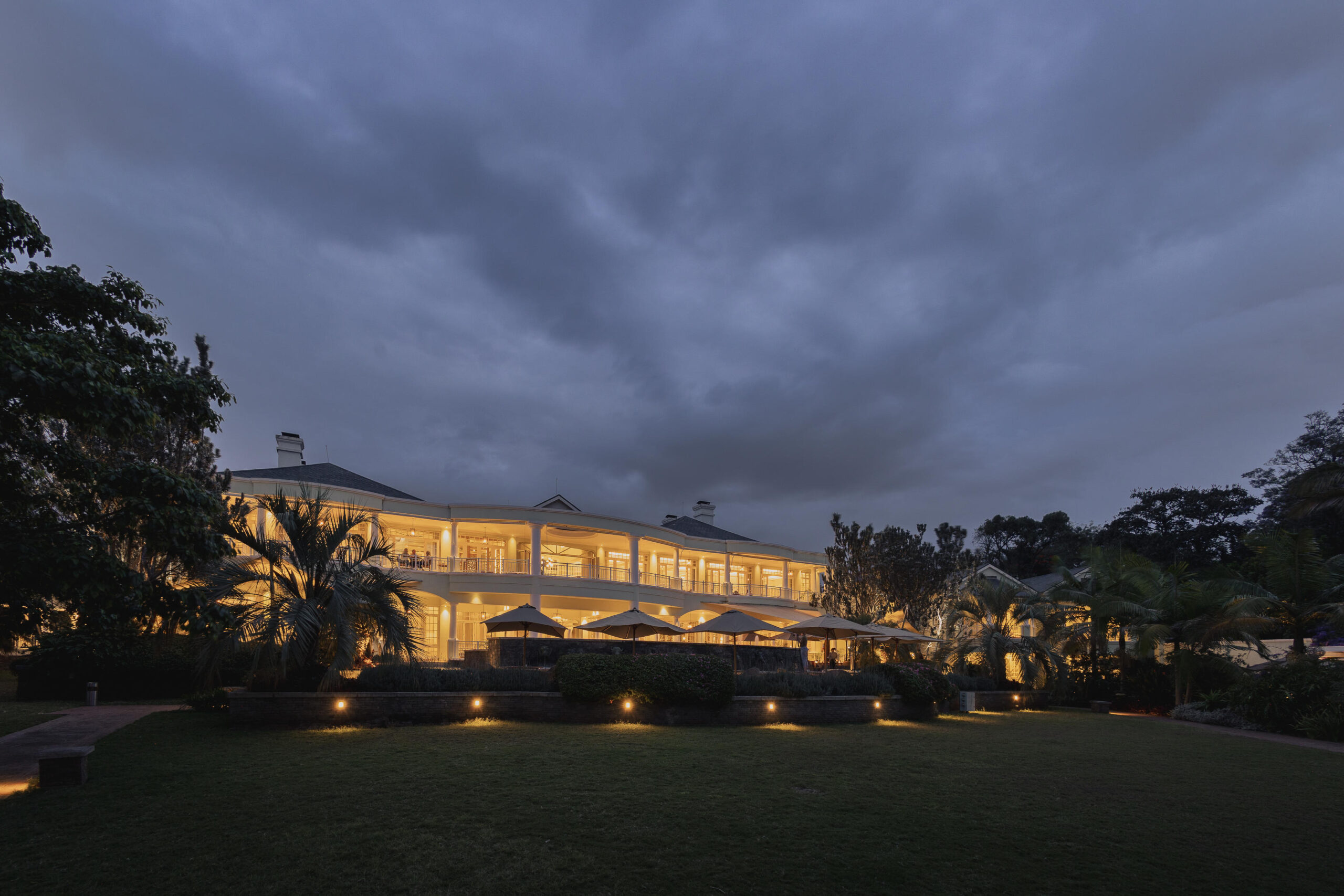 Exterior and Gardens - Go Do Africa Two-story illuminated restaurant terrace at dusk with outdoor seating under umbrellas and palm trees nearby