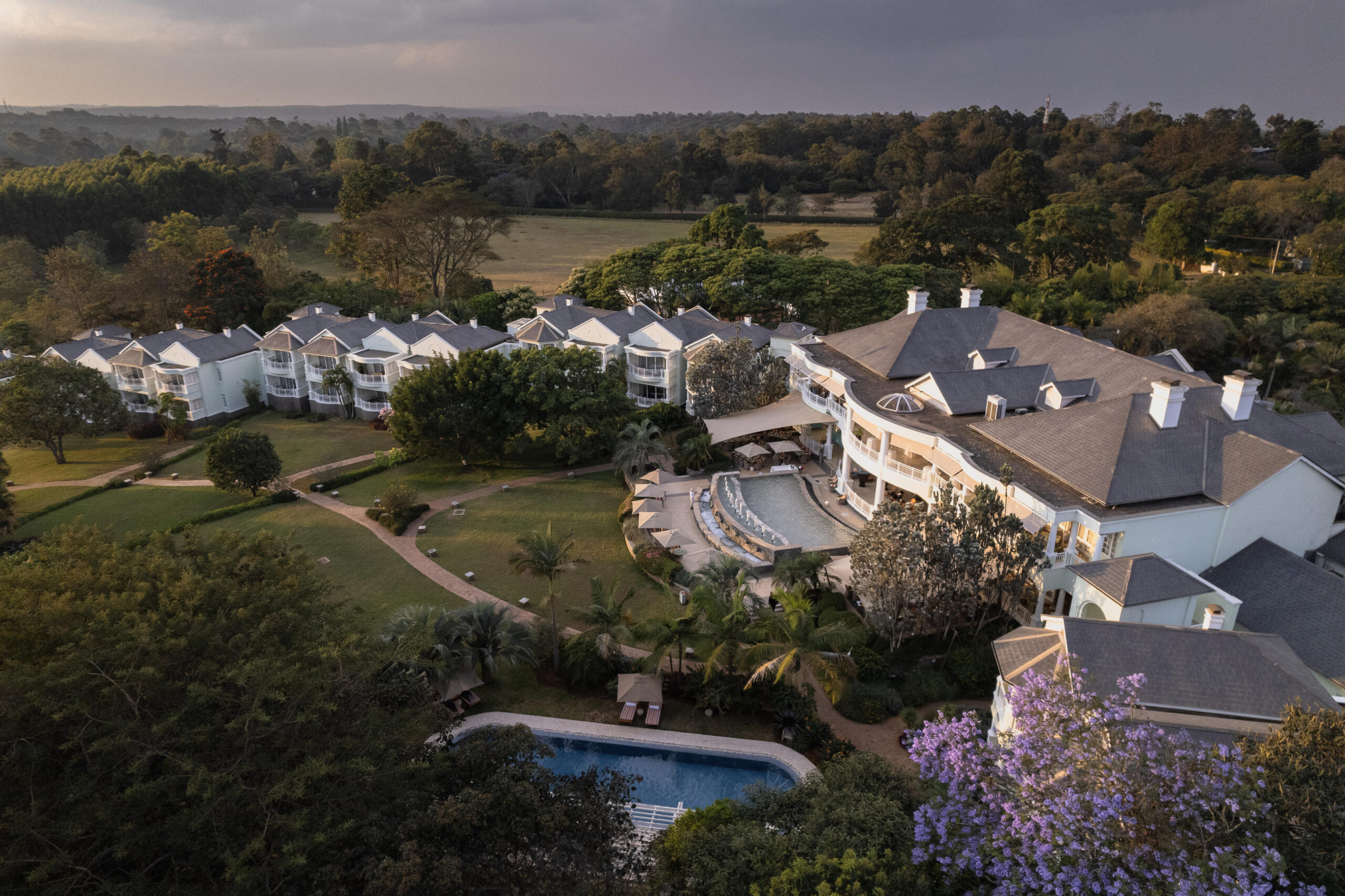 Property Aerial View - Go Do Africa Aerial view of a luxury resort with a curved central building, pool, and manicured gardens among trees and lawns.